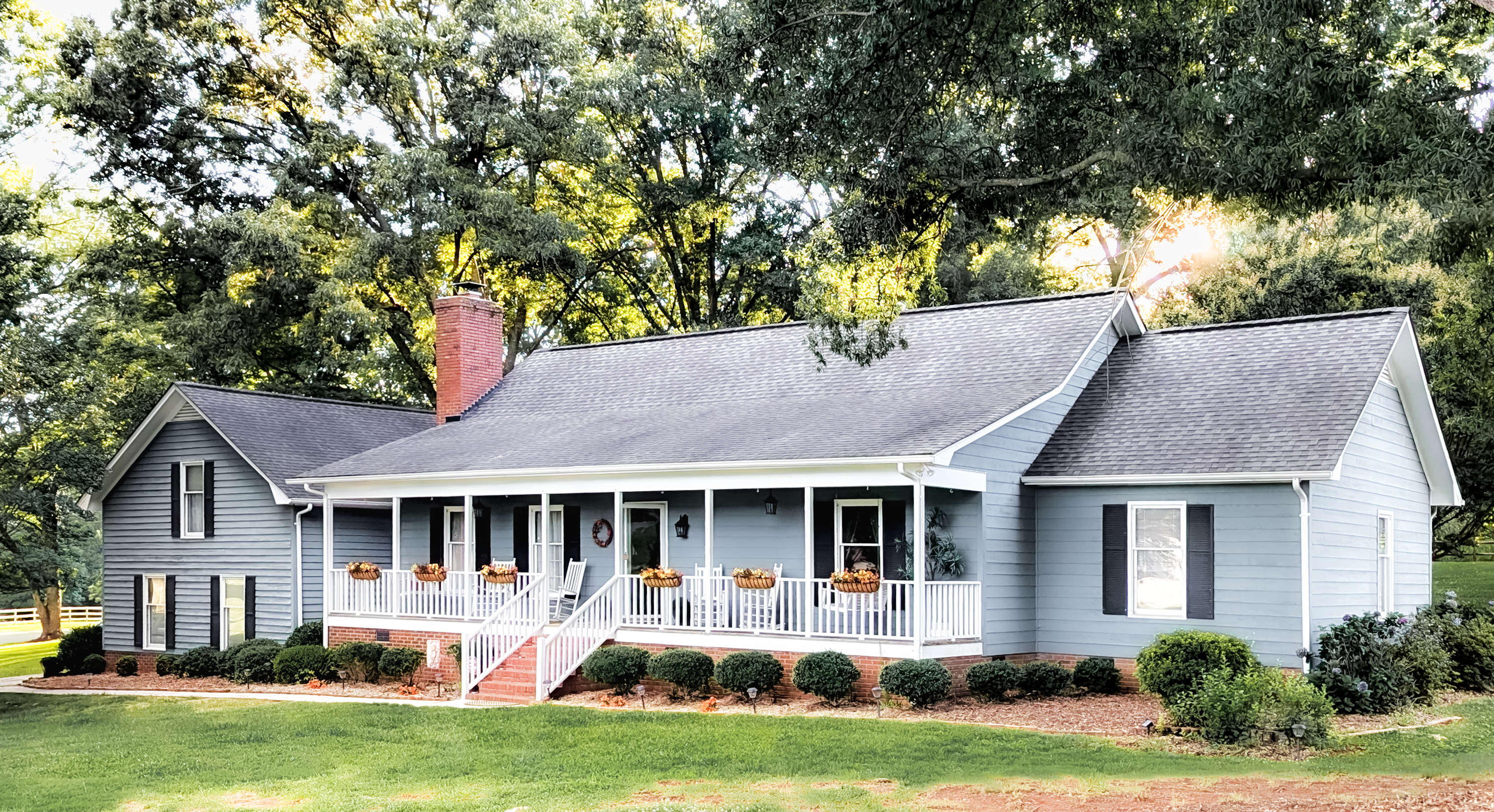 Front exterior of 9319 Old Gold Mine Court, a blue Cape Cod home with a wide covered porch framed by mature oaks