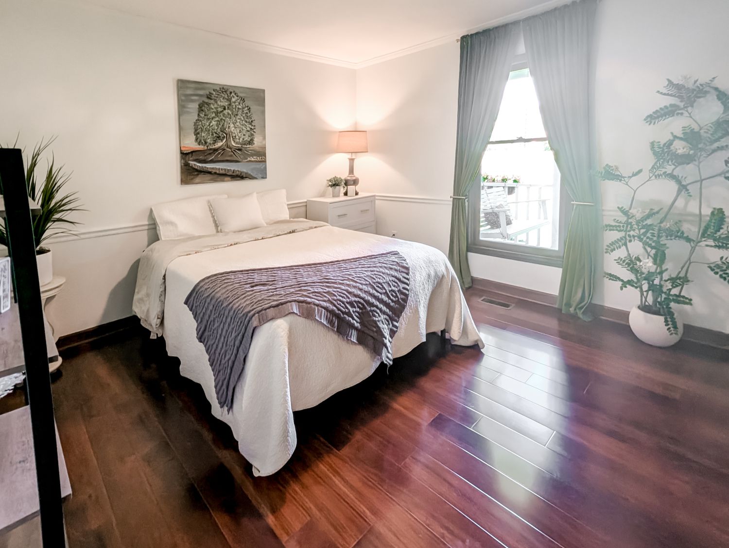 Serene guest bedroom with white bedding, a framed tree-of-life painting and hardwood floors